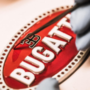 The word 'Bugatti' is carved in black and white 3D-style letters within the crimson oval, with the stylized EB emblem atop it. The logo exudes luxury and elegance.